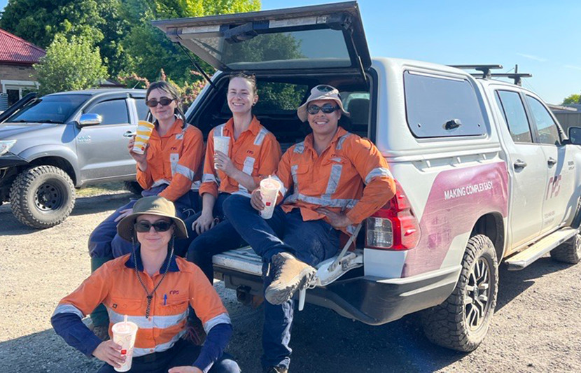 The RPS ecology team rest behind the RPS logoed truck all wearing orange high-vis, hiking boots, and holding drinks. The team are made up of three females and one male member. 